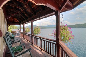 Eine überdachte Terrasse mit Holzbalkonen, grünen Stühlen und hängenden Blumenkörben mit Blick auf einen See.
