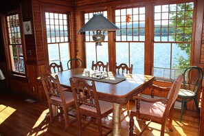 Ein Esszimmer mit Holzboden, einem Tisch und Stühlen, großen Fenstern mit Seeblick und einer Hängelampe.