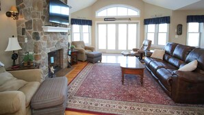 A spacious living room with a stone fireplace, leather sofa, and a large window with curtains. - Surf City Oceanfront Property (Surf City)