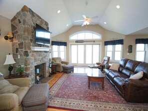 A spacious living room with a stone fireplace, leather sofa, and a large window with curtains. - Surf City Oceanfront Property (Surf City)
