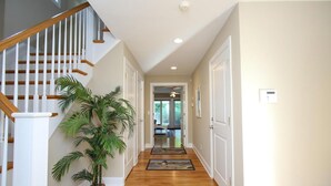 A hallway with wooden flooring, white walls, a staircase with wooden railings, and a potted plant. - Surf City Oceanfront Property (Surf City)
