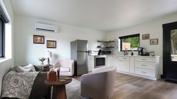 A modern kitchen with white cabinetry, stainless steel appliances, and a large window providing a view of the outdoors. - Steps from the Lake- Sauna + Hot Tub. Unit #2 (Jones)