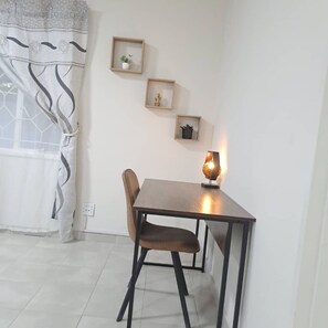 Een eethoek met een tafel, stoelen, een lamp en drie wandplanken met planten.