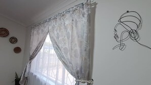 A room with a window covered by sheer curtains, a wall with a line drawing, and a tiled floor.