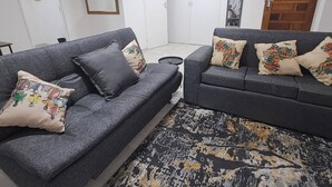 A living room with two grey sofas, patterned cushions, a black and gold rug, and a wooden door.