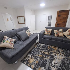 A living room with two grey sofas, patterned cushions, a black and gold rug, and a wooden door.