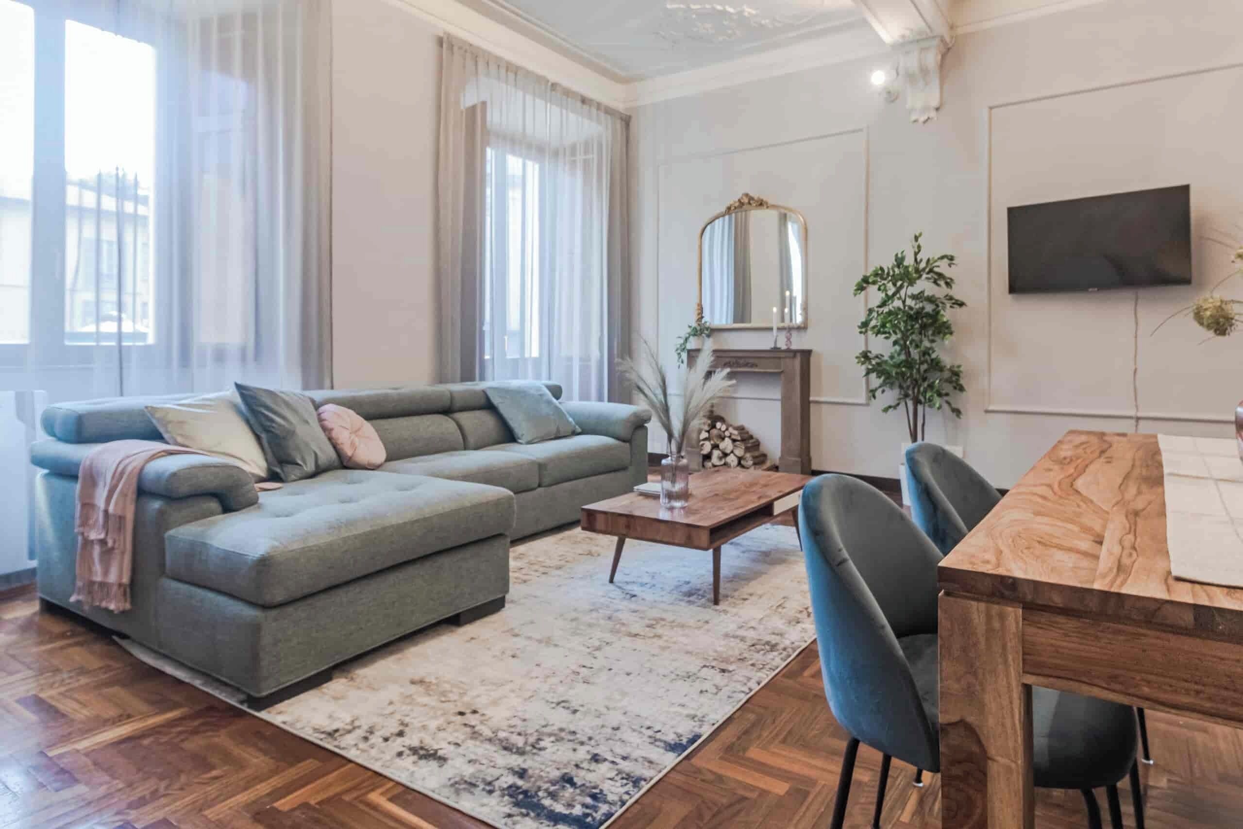 Een moderne woonkamer met een grijze modulaire bank, een houten salontafel, en een eethoek met een houten tafel en stoelen.