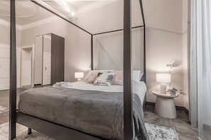 A four-poster bed with a grey bedspread, bedside tables with lamps, and a mirror on the wall. - [Como Historic Center] White Lotus Luxury Suites (Como)