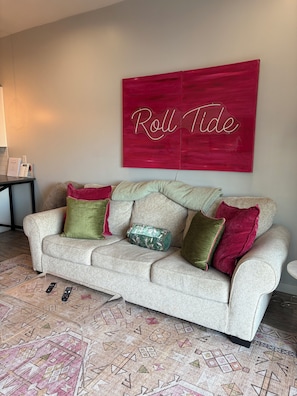 A beige sofa with multiple cushions, a patterned rug, and a red sign on the wall.