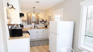A compact kitchen with white cabinets, a wooden dining table, and a refrigerator. - Thompson Cottage - Sleeps 4 (Sedro-Woolley)