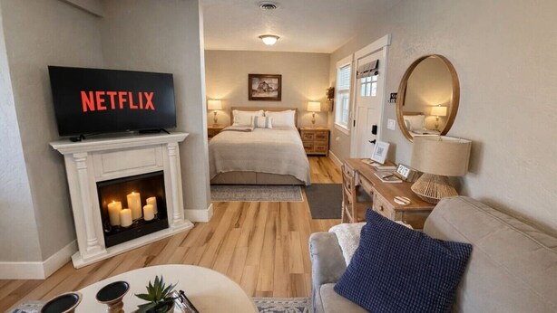 A hotel room with a fireplace, a bed, a desk, a TV, and a mirror. - Thompson Cottage - Sleeps 4 (Sedro-Woolley)
