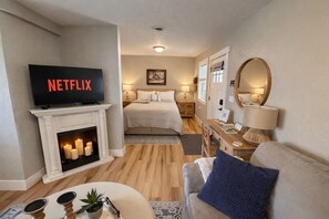 A hotel room with a fireplace, a bed, a desk, a TV, and a mirror.