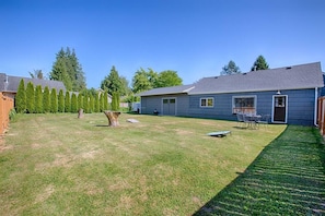 A residential backyard with a lawn, a tree stump, and a patio area with outdoor furniture.