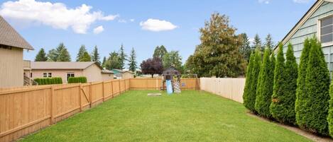 A backyard with a wooden fence, a small play structure, and a well-maintained lawn.