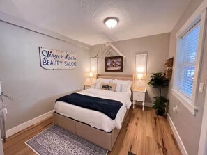 Quarto com cama, mesas de cabeceira, tapete, placa na parede e janela.