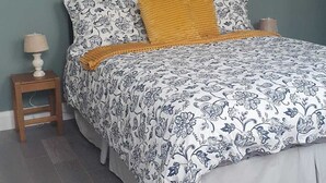 Ein Schlafzimmer mit einem Bett, einem Nachttisch, einer Lampe, einem gerahmten Bild an der Wand und einer Pendelleuchte.