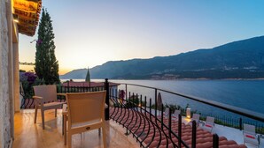 Un balcon avec des chaises, une balustrade et une vue sur une étendue d’eau et des montagnes.