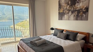 Une chambre avec un grand lit, une vue sur un plan d’eau et un tableau accroché au mur.