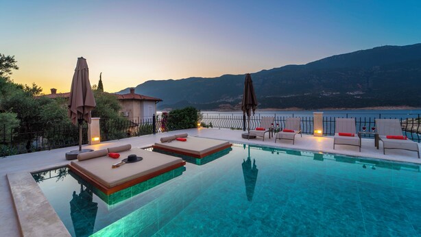 Un espace aménagé au bord de la piscine, avec des chaises longues et des parasols, offrant une vue sur un plan d’eau et des montagnes.