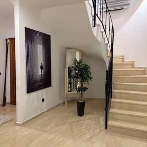 A staircase with a black handrail, a potted plant, and a framed mirror.