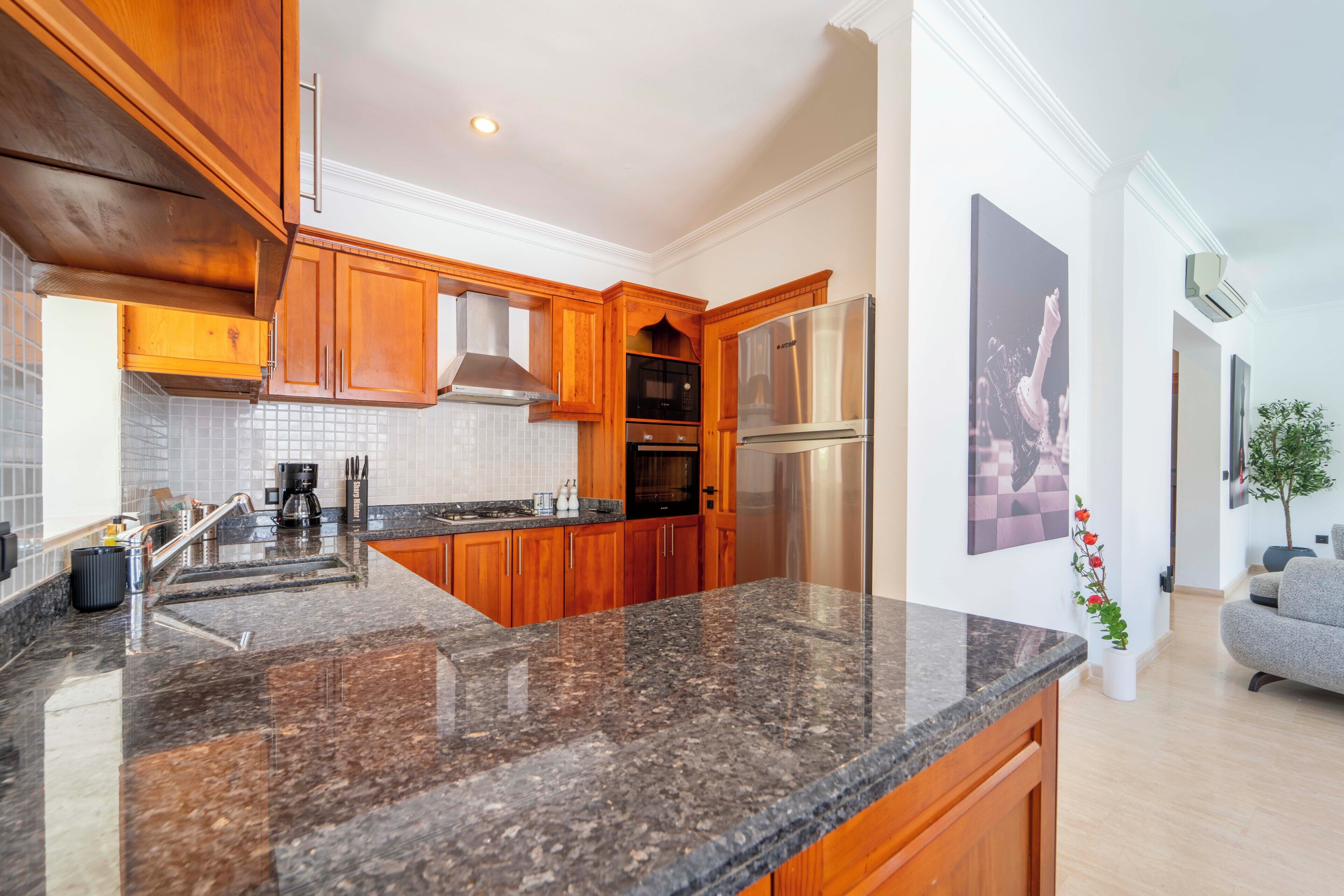 A modern kitchen with granite countertops, wooden cabinets, stainless steel appliances, and a tiled backsplash.