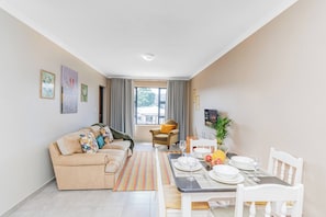 Ein Wohnzimmer mit einer Couch, einem Esstisch, Stühlen und einem Fenster mit Vorhängen.