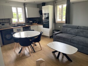A compact kitchen with modern appliances, a dining area with a marble table, and a grey sofa.