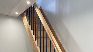 En trætrap med sorte gelændere, en hvid væg og et sort flisegulv.