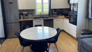 Et moderne køkken med en central ø, integrerede hårde hvidevarer og et spiseområde med et rundt bord og stole.