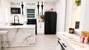 Une cuisine moderne avec des meubles blancs, un réfrigérateur noir et un îlot central en marbre.