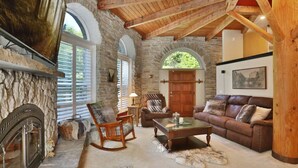 Ein rustikales Interieur mit Steinwänden, Kamin, Holzmöbeln und einem großen Fenster.