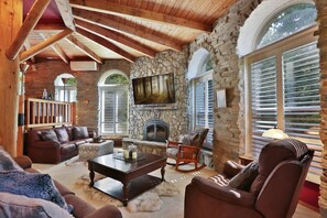 A cozy living room with stone walls, a fireplace, wooden beams, and large windows. - Wiseman Castle- Beautiful Waterfalls! (Sedro-Woolley)