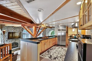A modern kitchen with a stone fireplace, wooden beams, and a large island. - Wiseman Castle- Beautiful Waterfalls! (Sedro-Woolley)