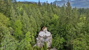 Eine burgähnliche Struktur, umgeben von dichtem Wald, mit freiem Blick auf die umliegenden Berge.