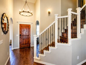 Un escalier avec des rampes blanches et des balustres noires, une porte en bois et un lustre.