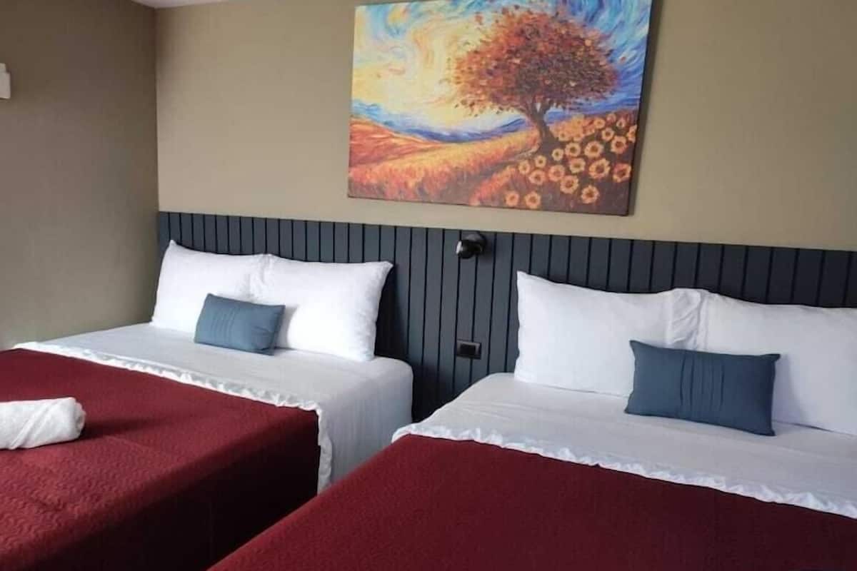 Hotellihuone, jossa on kaksi sänkyä, seinällä oleva taulu, jossa on kuvattuna puu ja kukkia, sekä ikkuna.
