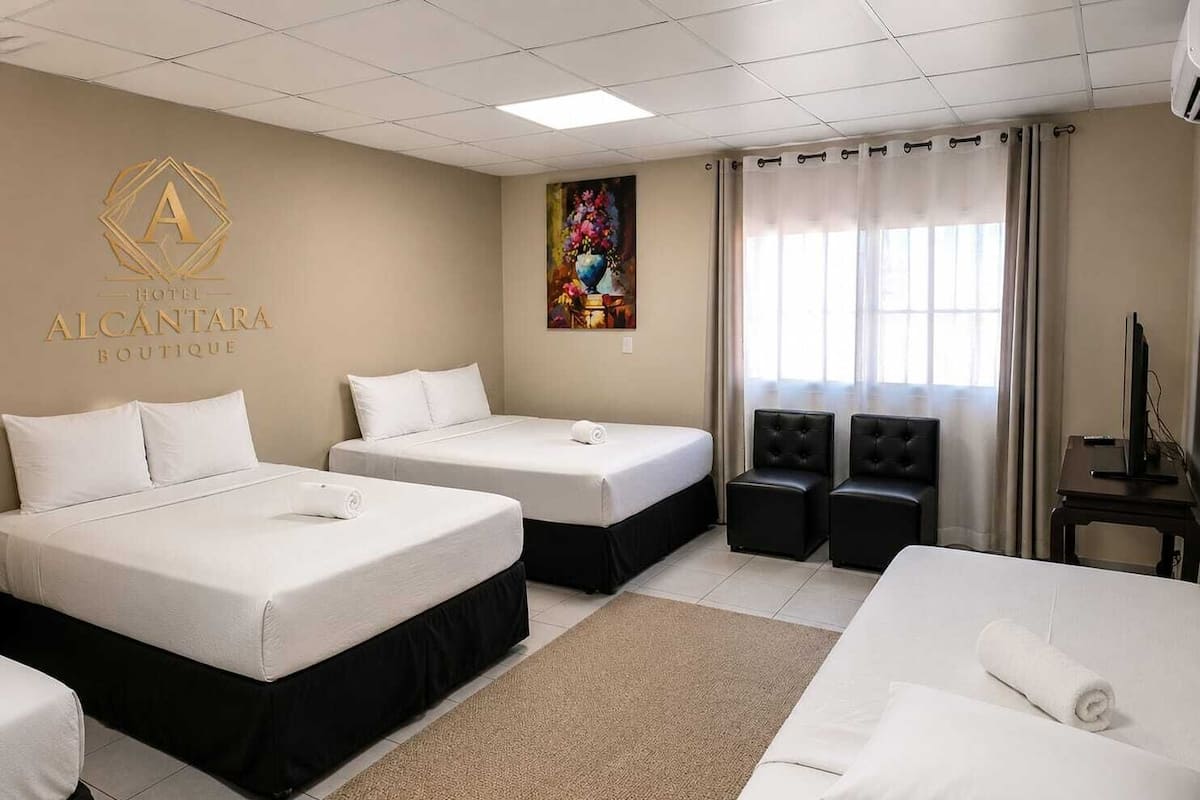Hotellihuone, jossa on kaksi sänkyä, sohva, televisio ja taulu seinällä.