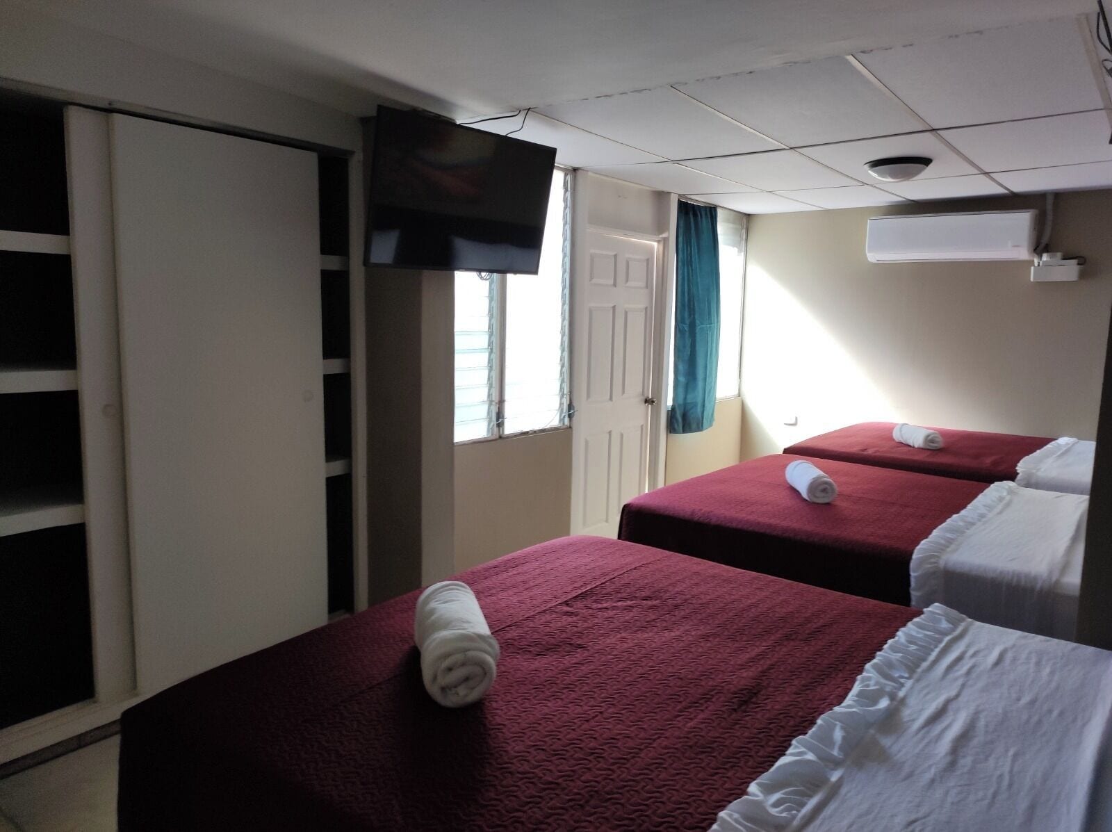 A hotel room with two beds, a TV, a wardrobe, and a window with curtains.