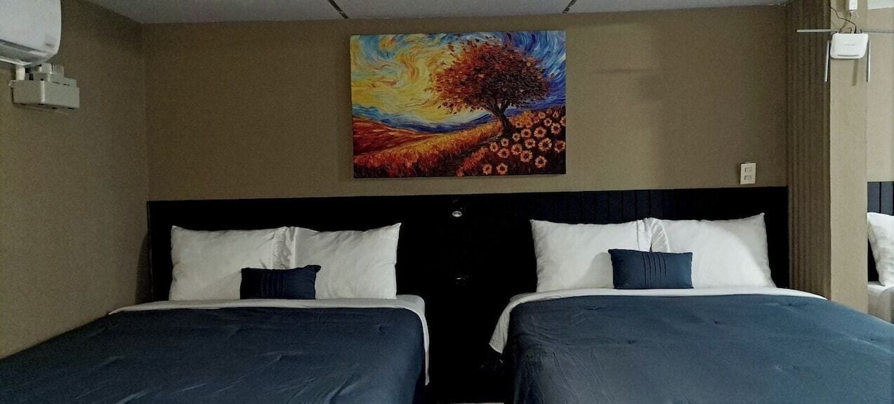 A hotel room with two beds, a large painting on the wall, and a window with curtains.