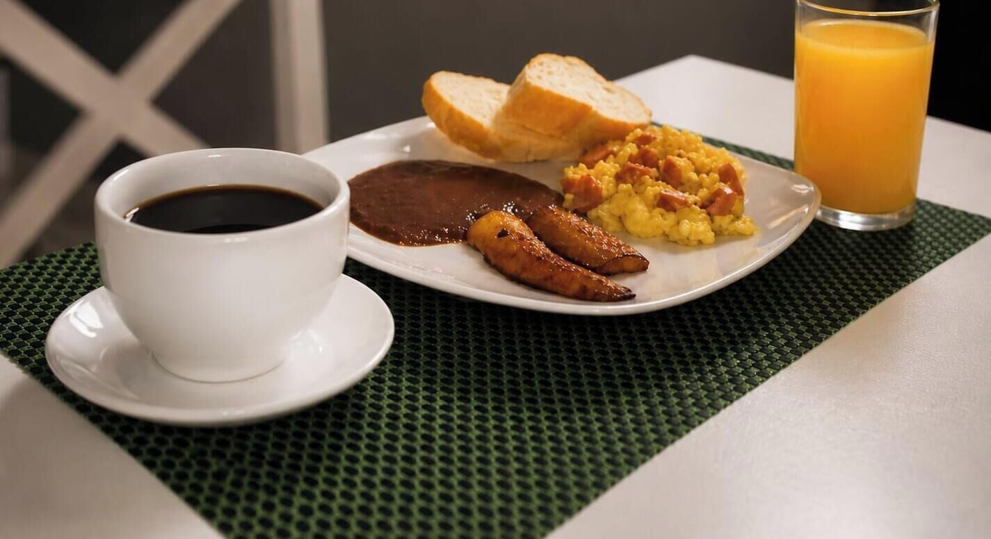 A breakfast plate with eggs, sausage, and toast, a cup of coffee, and a glass of orange juice on a table.