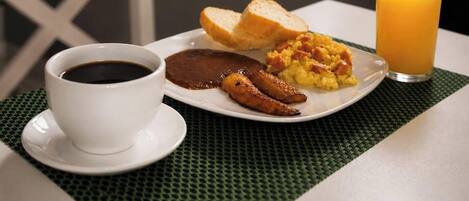 A breakfast plate with eggs, sausage, and toast, a cup of coffee, and a glass of orange juice on a table.