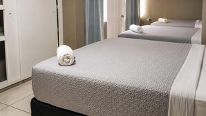 Una habitación de hotel con dos camas, un almohadón azul y una toalla enrollada sobre la primera cama.