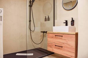 Une salle de bain moderne avec une douche à parois de verre, un meuble-lavabo en bois avec un lavabo blanc et un miroir rond.