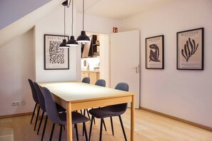 A dining area with a wooden table and chairs, framed artwork on the walls, and pendant lighting.