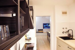 A modern kitchen with a black range hood, a sink, and a TV in the background.