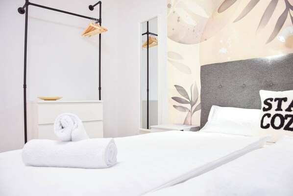 Une chambre d’hôtel avec un lit, une serviette, une table de chevet, un miroir et un mur orné d’un motif de feuilles.