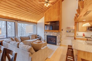 Una sala de estar acogedora con chimenea de piedra, un televisor plano grande y techo de madera.
