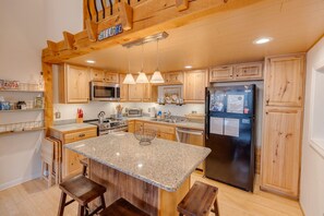 Una cocina amplia con armarios de madera, encimeras de granito, una isla central y un refrigerador de acero inoxidable.