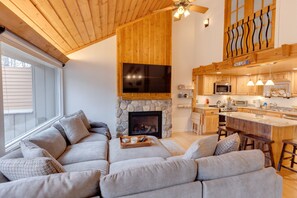 Una sala de estar acogedora con chimenea de piedra, un televisor grande y techo de madera.