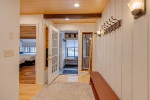 Un pasillo con un banco de madera, un perchero y una puerta que da a un dormitorio con cama y ventana.
